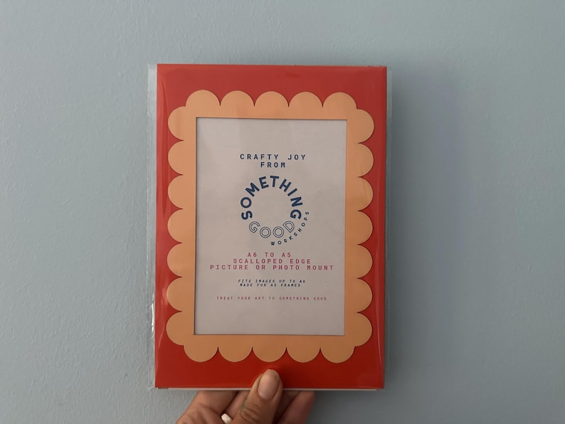 May include: A red picture frame with a scalloped edge and a peach-colored interior. The frame contains text that reads "Crafty Joy From Something Good Workshop" and "As To As Scalloped Edge Picture or Photo Mount."