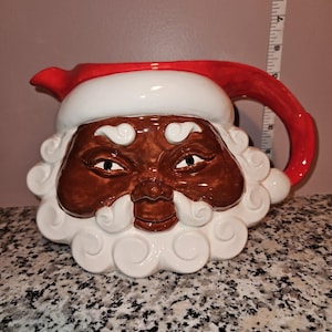 May include: A ceramic Santa Claus pitcher with a red handle and spout. The pitcher features a white beard and hat trim, a brown face, and a red hat. The pitcher is approximately 9 inches tall.