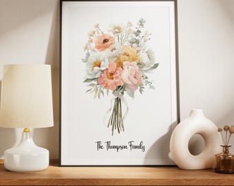 Könnte beinhalten: Ein gerahmter Blumendruck mit einem Aquarellstrauß aus pfirsichfarbenen, rosa, gelben und weißen Blumen. Der Text "The Thompson Family" ist darunter gedruckt. Das Kunstwerk wird auf einer Holzoberfläche präsentiert.