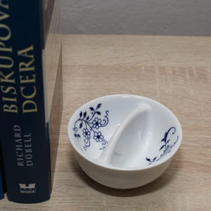 Peut inclure: Bol divisé blanc avec un motif floral bleu. Le bol a un séparateur incurvé et est décoré de fleurs et de feuilles bleues. Le bol est posé sur une surface en bois clair.