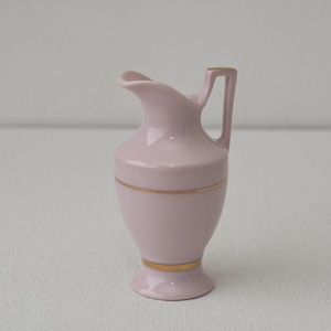 Può includere: Un piccolo brocca in ceramica rosa con manico e beccuccio. La brocca ha una fascia dorata attorno alla parte superiore e inferiore. La brocca è alta circa 13 cm.