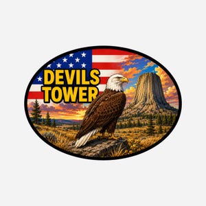 Op de afbeelding: Ovale sticker met een Amerikaanse zeearend en de tekst "DEVILS TOWER". De achtergrond toont de Amerikaanse vlag, een schilderachtig uitzicht op Devils Tower en een zonsondergang.