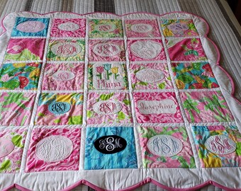 May include: A pink and white quilt with a scalloped edge. The quilt is made up of 25 squares, each with a different floral pattern. The squares are embroidered with various initials in a black oval.