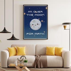 May include: A framed print with a cartoon moon smiling against a starry night sky. The text reads "I'M OVER THE MOON FOR MATH" in a pixelated font. The print is above a beige sofa with yellow cushions.
