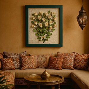 以下が含まれることがあります： クリーム色のバラと緑の葉のブーケが描かれた、額入りの花の壁掛けアート。 作品は、濃い緑色のフレームの中に、テクスチャ加工された背景に配置されています。 オレンジと茶色の装飾的なクッションがベージュのソファを飾っています。