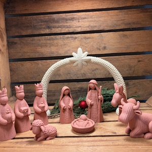 Könnte beinhalten: Ein Krippenset in Terrakotta-Farbe mit stilisierten Figuren, die eine texturierte, strickähnliche Oberfläche aufweisen. Das Set besteht aus drei Königen, einem Hirten, einer Figur mit Kopfbedeckung, einem Baby in der Krippe, einem Schaf und einer Kuh.