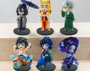 Puede incluir: Un conjunto de seis figuras chibi de estilo anime sobre bases circulares negras. Los personajes lucen atuendos variados, incluyendo kimonos y haoris, con accesorios como paraguas azules y morados. Una figura aparece sin camisa con detalles azules.