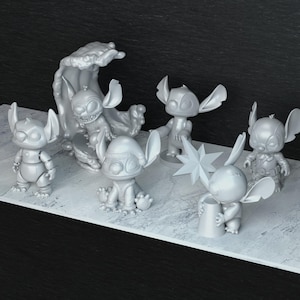 Peut inclure: Collection de six figurines grises du personnage Stitch du film Disney Lilo & Stitch. Les figurines sont dans diverses poses, dont une sur une vague et une autre tenant une &eacute;toile.