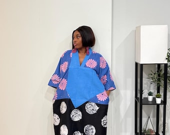 May include: A midi-length dress featuring a blue upper section with pink floral patterns and a V-neckline. The lower section is black with large white circular motifs. The garment has wide sleeves and a loose, flowing silhouette.