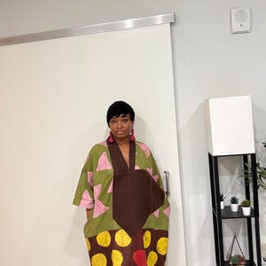 K&ouml;nnte beinhalten: Ein weit geschnittenes, knielanges Kleid mit Color-Blocking-Design. Der obere Teil ist olivgr&uuml;n mit rosa Dreiecksmustern, w&auml;hrend der untere Teil braun mit gro&szlig;en gelben und roten kreisf&ouml;rmigen Punkten bedruckt ist.