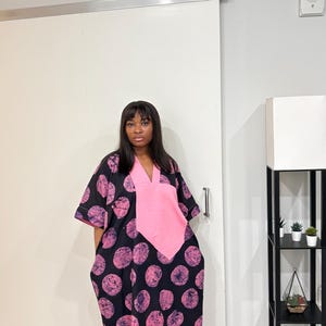 K&ouml;nnte beinhalten: Ein locker sitzendes schwarzes Kaftan-Kleid mit einem sich wiederholenden Muster aus texturierten rosa Kreisformen. Das Kleidungsst&uuml;ck verf&uuml;gt &uuml;ber einen einfarbigen rosa V-Ausschnitt, kurze weite &Auml;rmel und einen geraden Saum bis zur Wadenmitte.