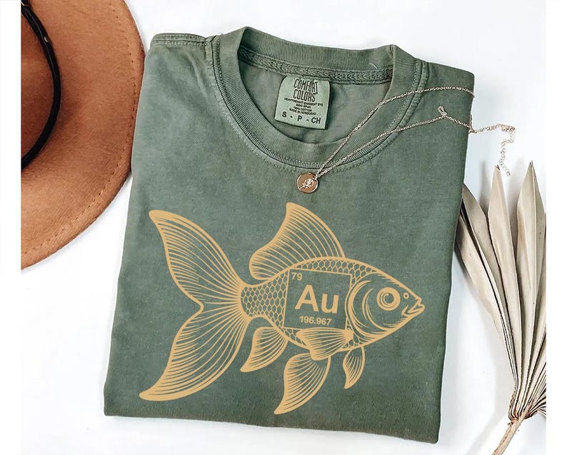 a green t-shirt with a gold fish graphic and the element Au (gold) printed on it, along with a necklace and a hat.