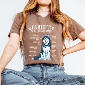 A woman wearing a brown t-shirt with an illustration of a Siberian Husky and text describing the anatomy of the breed.