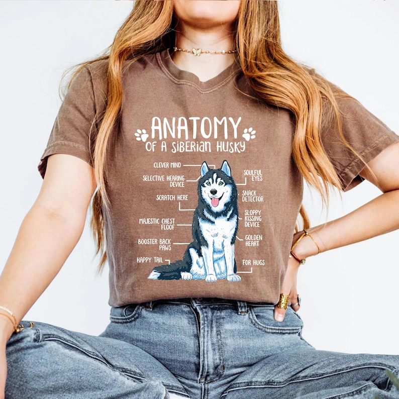 A woman wearing a brown t-shirt with an illustration of a Siberian Husky and text describing the anatomy of the breed.