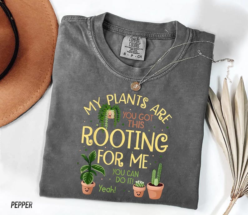 a gray t-shirt with a humorous text and illustrations of potted plants, along with a necklace and a hat.