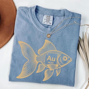 a blue t-shirt with a yellow fish design, a brown hat, and a necklace, all placed on a white surface.