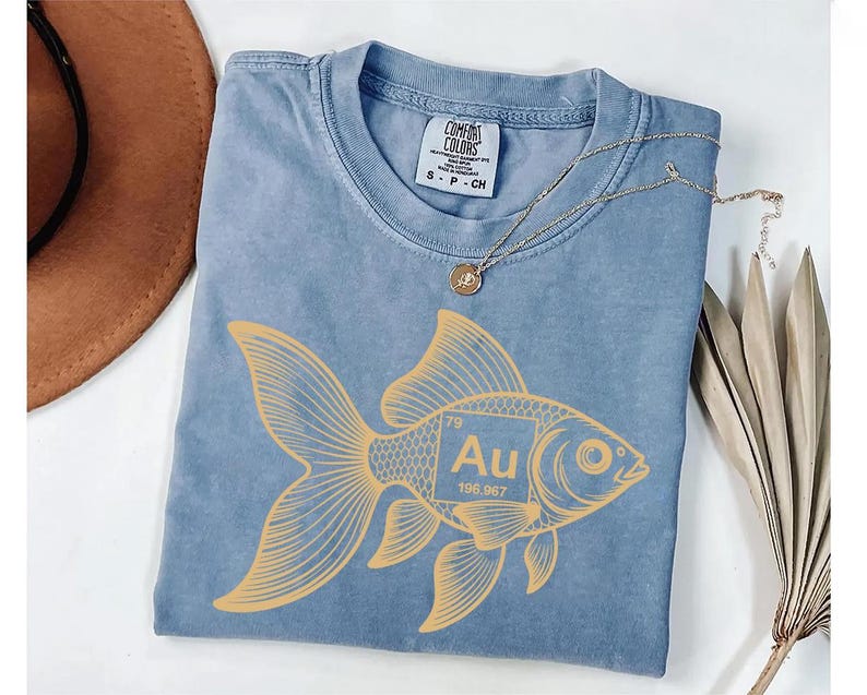 a blue t-shirt with a yellow fish design, a brown hat, and a necklace, all placed on a white surface.