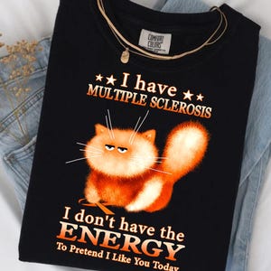 May include: Black t-shirt with the text "I have Multiple Sclerosis" and "I don't have the ENERGY To Pretend I Like You Today." The shirt features an orange cartoon cat with an annoyed expression.