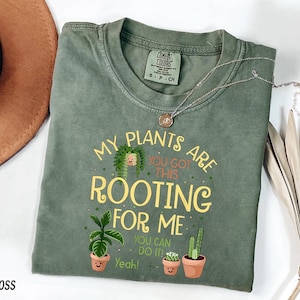 a green t-shirt with a playful message about plants, a brown hat, and some dried leaves, all arranged on a white background.
