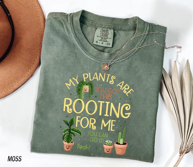 a green t-shirt with a playful message about plants, a brown hat, and some dried leaves, all arranged on a white background.