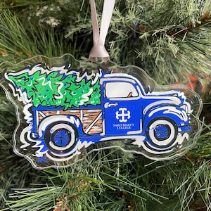 May include: A blue pickup truck with a Christmas tree in the bed. The truck has a white roof and a white stripe down the side. The truck has a Saint Mary's College logo on the side. The truck is a Christmas ornament.