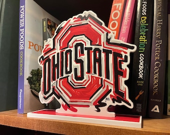 May include: A red, white, and black Ohio State logo with a white background. The logo is a stylized letter "O" with a star inside. The words "Ohio State" are written in black letters below the "O".