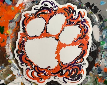May include: Orange and purple paw print with a white background and a black and purple swirl design around the paw print. The design is on a white background.