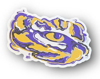 May include: A purple and gold abstract design of a tiger's eye. The design is stylized and has a swirling, liquid-like appearance. The eye is outlined in black and has a white pupil. The design is on a white background.