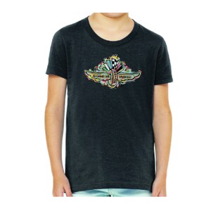 Puede incluir: Una camiseta gris oscuro para ni&ntilde;os con un gr&aacute;fico colorido del logotipo del Indianapolis Motor Speedway. El logotipo presenta un neum&aacute;tico estilizado con alas y el texto "Indianapolis Motor Speedway".