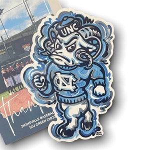 May include: A blue and white cartoon mascot sticker with a ram's head and the letters "UNC" on its hat. The mascot is wearing a blue and white jersey with the letters "UNC" on the front. The sticker is on a white background.