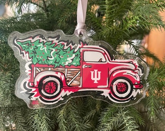 May include: A red truck with a Christmas tree in the bed. The truck has a white "IU" logo on the side. The truck is a Christmas ornament.