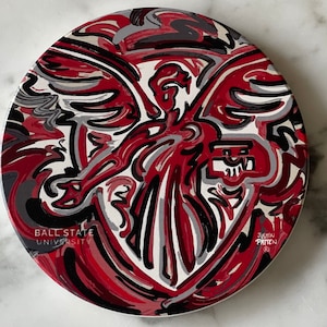 May include: A red, white, and black abstract design with a stylized angel figure. The design includes the text "Ball State University" and "Justin Patten".