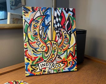 Może przedstawiać: Kolorowy, abstrakcyjny obraz przedstawiający stylizowane logo Indy 500 z napisami "Indianapolis Motor Speedway" i "Indy 500".