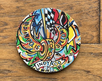 Może przedstawiać: Okrągły, kolorowy podkładka z graficznym wzorem przedstawiającym logo Indianapolis Motor Speedway, słowa "Indy 500" i podpis artysty "Justin Patten".