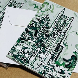 May include: A green and white illustrated greeting card featuring a tall building with a clock tower and a tree in the foreground. The card has a white envelope.