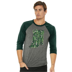 May include: A heather grey and forest green baseball tee shirt with a graphic of the state of Indiana. The graphic is made up of the words "Zionsville" in a green camouflage pattern.