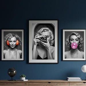 May include: Three framed black and white prints of a woman with blonde curly hair. One print shows her wearing orange headphones, another holding a camera, and the third blowing a bubble. The prints are displayed above a wooden dresser.