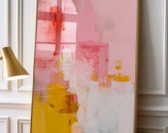 May include: A rectangular framed wall art piece featuring an abstract composition of layered paint strokes in shades of soft pink, vibrant yellow, and white, displayed in a thin gold frame on a wooden surface next to a gold desk lamp.