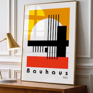 Può includere: Una stampa artistica Bauhaus incorniciata con forme geometriche in giallo, arancione, nero e rosso su sfondo bianco. La parola "Bauhaus" e l'anno "1923" sono stampati in basso. La cornice è dorata.