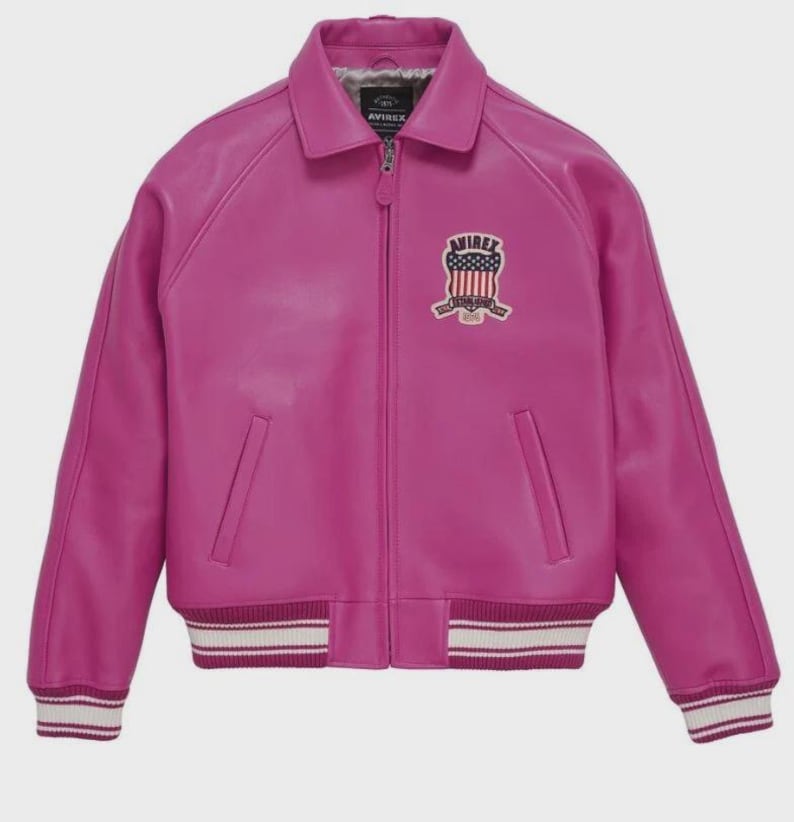 May include: A bright fuchsia leather jacket in a bomber style. It has a collared neckline, a zip-up front, and two front pockets. The jacket features a ribbed hem and cuffs with white and burgundy stripes. An "AVIREX" patch with an American flag design is on the chest.