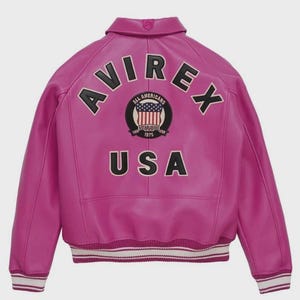 May include: A bright fuchsia leather jacket featuring the word "AVIREX" in black lettering across the shoulders. A circular emblem with "ALL AMERICANS ESTABLISHED 1975" and "USA" is also visible. The jacket has a ribbed hem with white and black stripes.