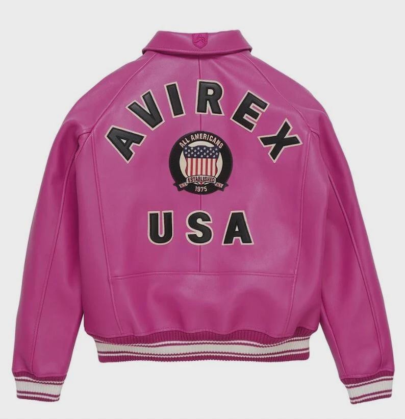 May include: A bright fuchsia leather jacket featuring the word "AVIREX" in black lettering across the shoulders. A circular emblem with "ALL AMERICANS ESTABLISHED 1975" and "USA" is also visible. The jacket has a ribbed hem with white and black stripes.