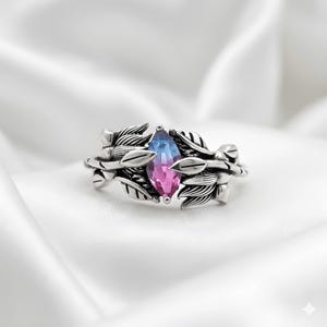 Può includere: Un anello d'argento con una gemma taglio marquise, che passa dal blu al rosa. L'anello è ornato da un dettagliato design a foglie. Il gioiello è posto su uno sfondo bianco.