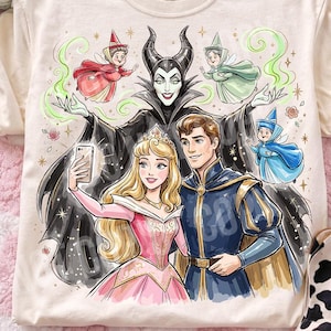 May include: Cream t-shirt with a colourful graphic of Disney characters, including Aurora, Prince Phillip, and Maleficent, taking a selfie. The design includes the text "ORIGINAL DESIGNER CALIGRAPHICDESIGN".