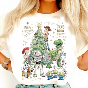 May include: White t-shirt featuring a colorful graphic of Toy Story characters decorating a Christmas tree. The design includes Woody, Buzz Lightyear, Rex, and the Little Green Men, with the text "Merry Christmas" and "Toy Story Holiday".