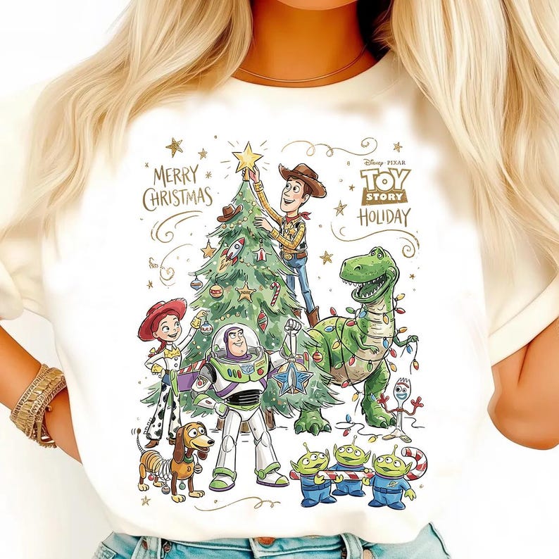 May include: White t-shirt featuring a colorful graphic of Toy Story characters decorating a Christmas tree. The design includes Woody, Buzz Lightyear, Rex, and the Little Green Men, with the text "Merry Christmas" and "Toy Story Holiday".