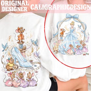 May include: White sweatshirt featuring a Cinderella-themed design. The design includes Cinderella in a blue gown, mice, birds, a glass slipper, and the text "ORIGINAL DESIGNER CALIGRAPHICDESIGN". The artwork is detailed with soft colors and whimsical elements.