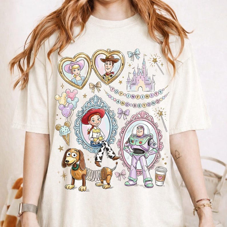 Może przedstawiać: Kremowa koszulka z kolorowymi ilustracjami postaci z Toy Story. Projekt zawiera Woody'ego, Buzz'a Astrala, Jessie i Slinky Dog, wraz z napisem "TO INFINITY AND BEYOND."