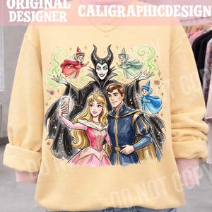 May include: A pale yellow sweatshirt with a vibrant illustration of a princess, a prince, and a villain posing for a selfie. The design includes fairies and the text "ORIGINAL DESIGNER CALIGRAPHICDESIGN".