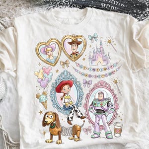 Może przedstawiać: Biała koszulka z kolorowymi ilustracjami postaci z Toy Story, w tym Chudego, Buzz'a Astrala i Jessie, w ozdobnych ramkach. Projekt zawiera zamek, balony i napis "TO INFINITY AND BEYOND."